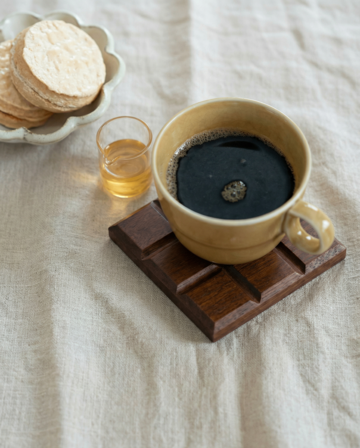 Dark wooden coaster under a coffee cup on a linen surface